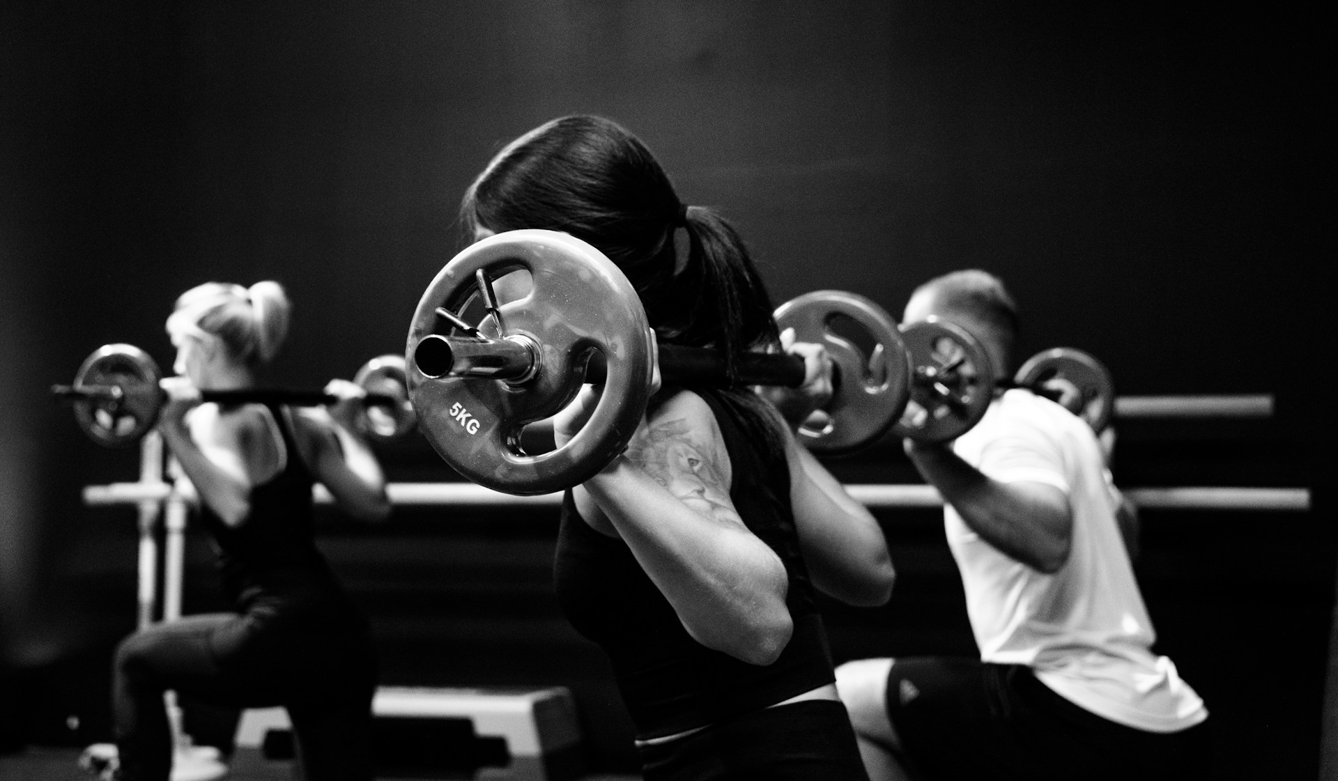 Black and white photo of three people lifting barbells.